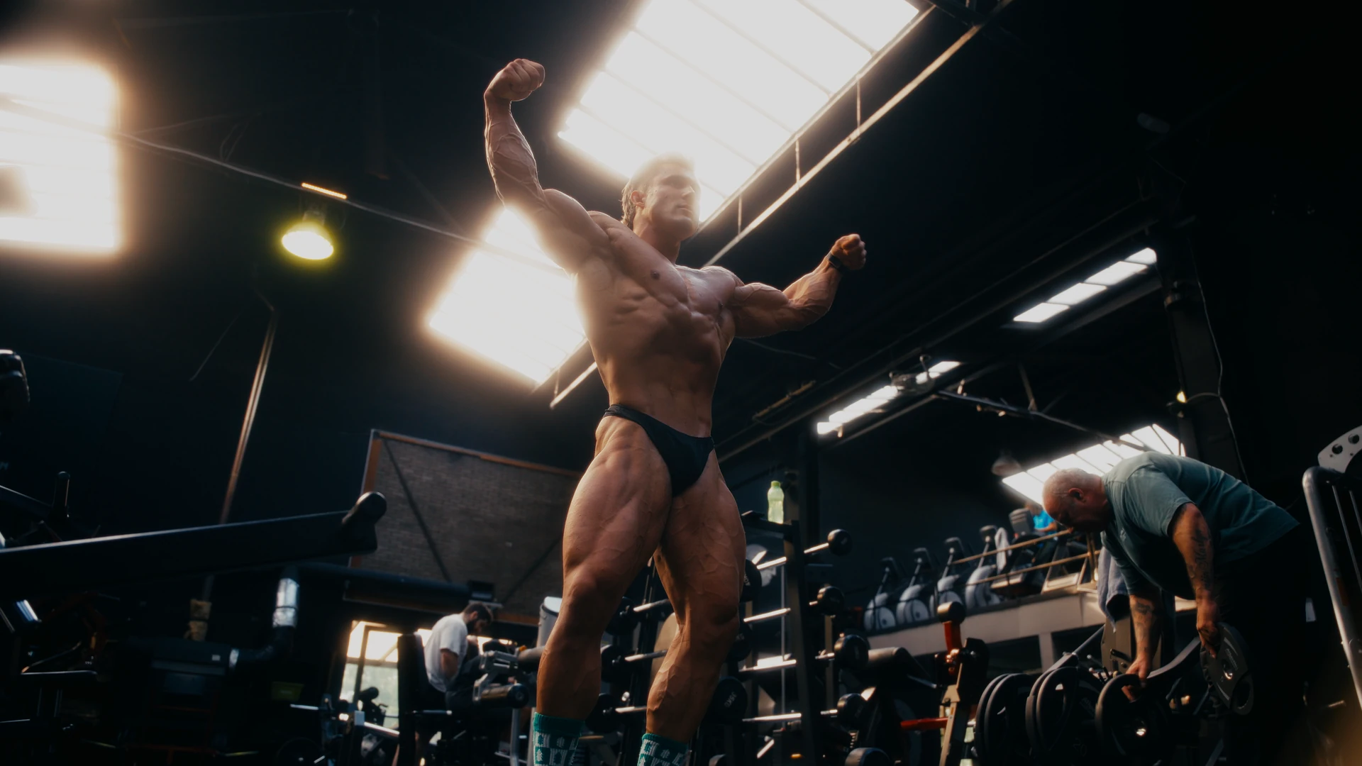 Bodybuilder poseert met geheven armen onder de dakramen van de gym